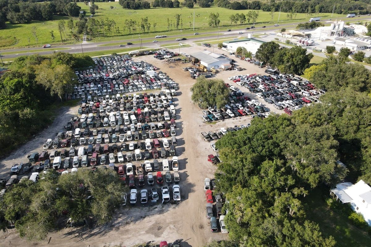 Budget U-Pull-It: Aerial view of a large salvage yard with rows of cars on dirt lots beside a highway and surrounded by trees