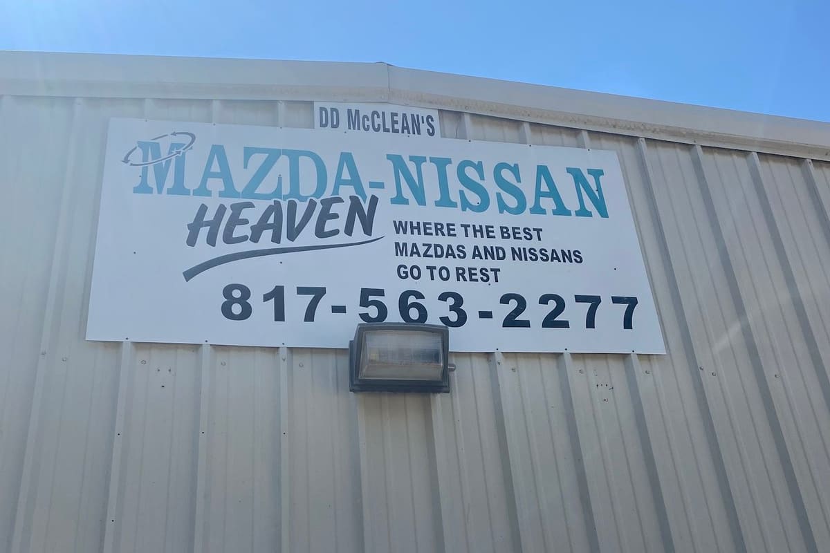 Fenix Parts EV: Large sign on a metal building reading Mazda-Nissan Heaven with a phone number, under a clear blue sky