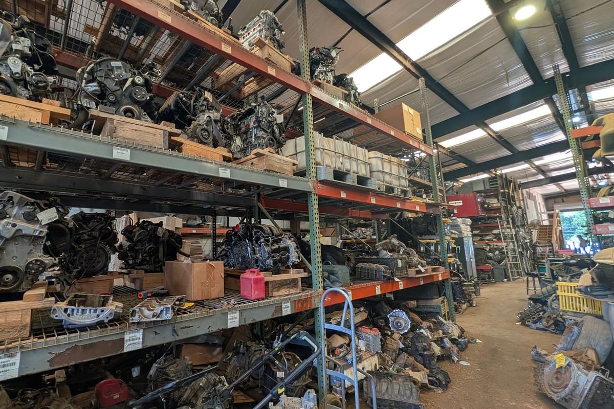 R. Stroud's: Covered warehouse with tall metal shelving racks full of used engines and transmissions, with more parts piled along the aisle