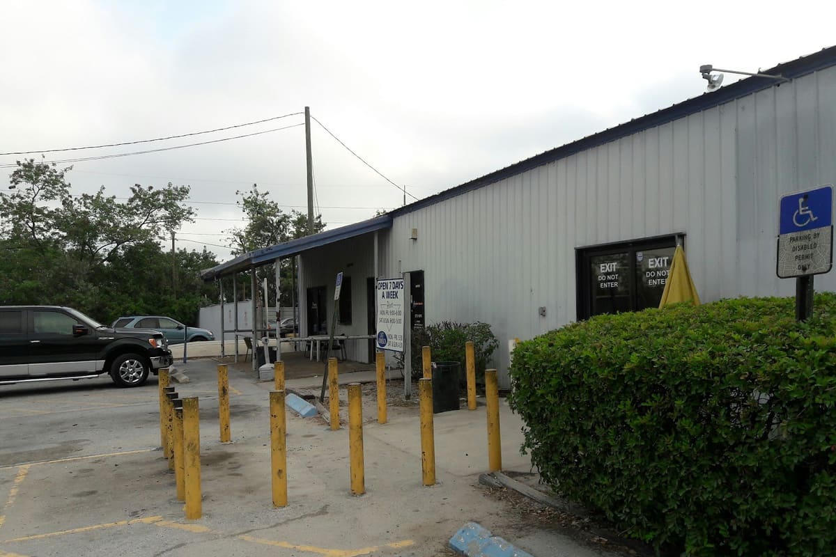 Pick Your Part - Clearwater: Metal office building with covered entrance, yellow posts and a parking lot with a handicap sign and green hedge