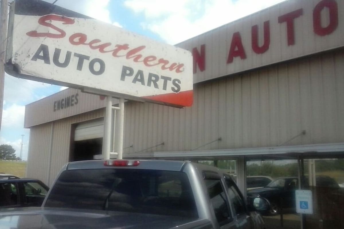Southern Auto Parts: Weathered auto parts sign in front of a tan metal building with an engines bay door and a pickup truck parked nearby