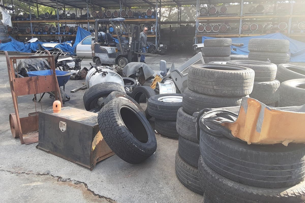Joseas Salvage Yard: Covered storage racks of engines and transmissions behind stacks of used tires and scrap parts on a paved salvage yard lot