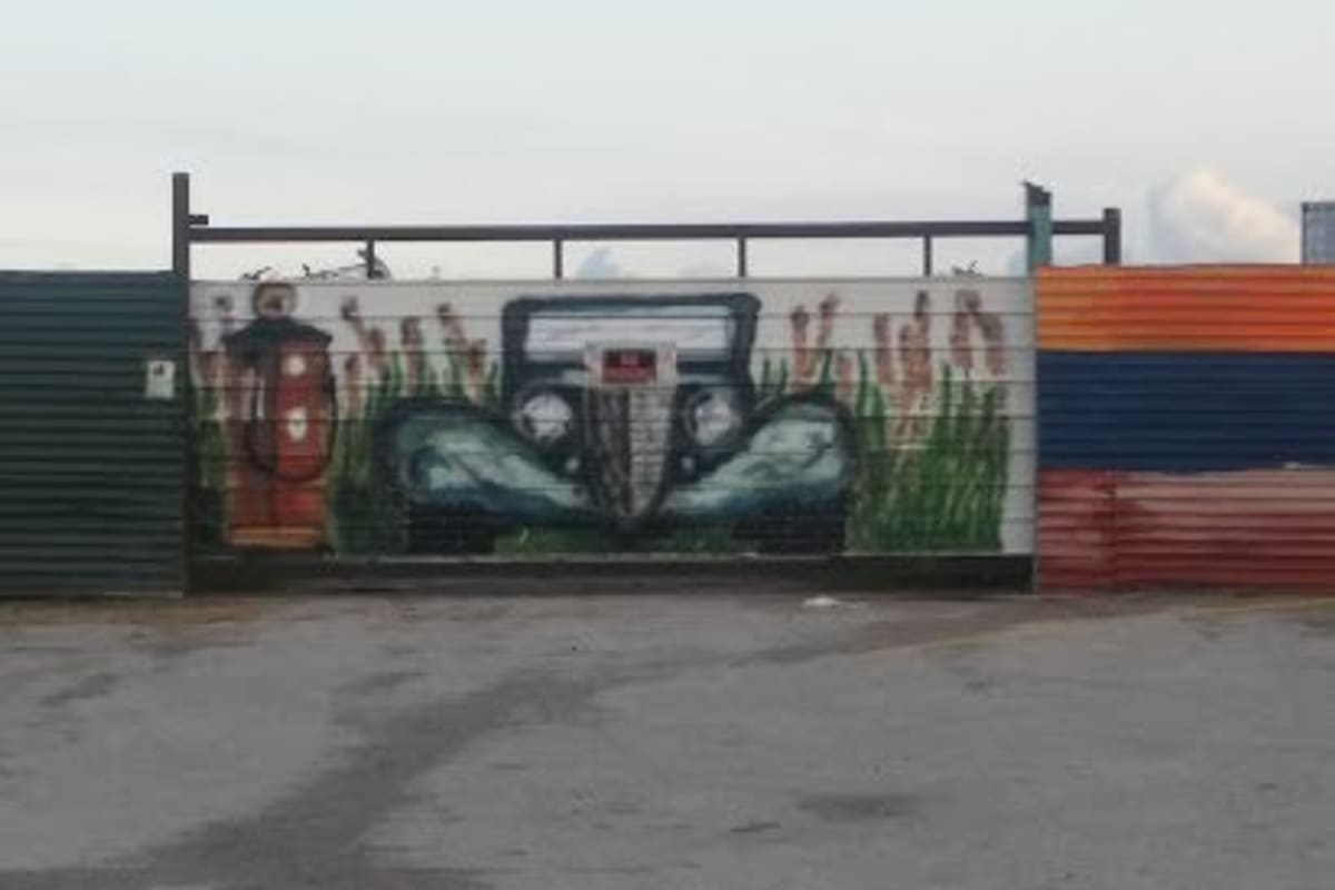Bay Area Auto Parts: Painted metal fence gate with a mural of a vintage car and gas pump, facing a concrete lot