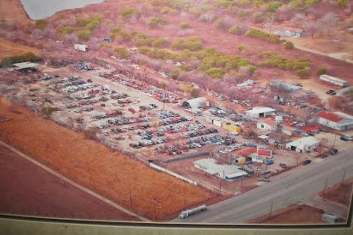 Nicks Auto Parts: Aerial view of a salvage yard with rows of cars, several small buildings, and a road along one side