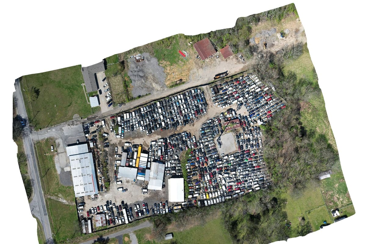 Neely's Bend Auto Salvage: Aerial view of a salvage yard with rows of vehicles packed beside large metal-roofed shop buildings and surrounding fields
