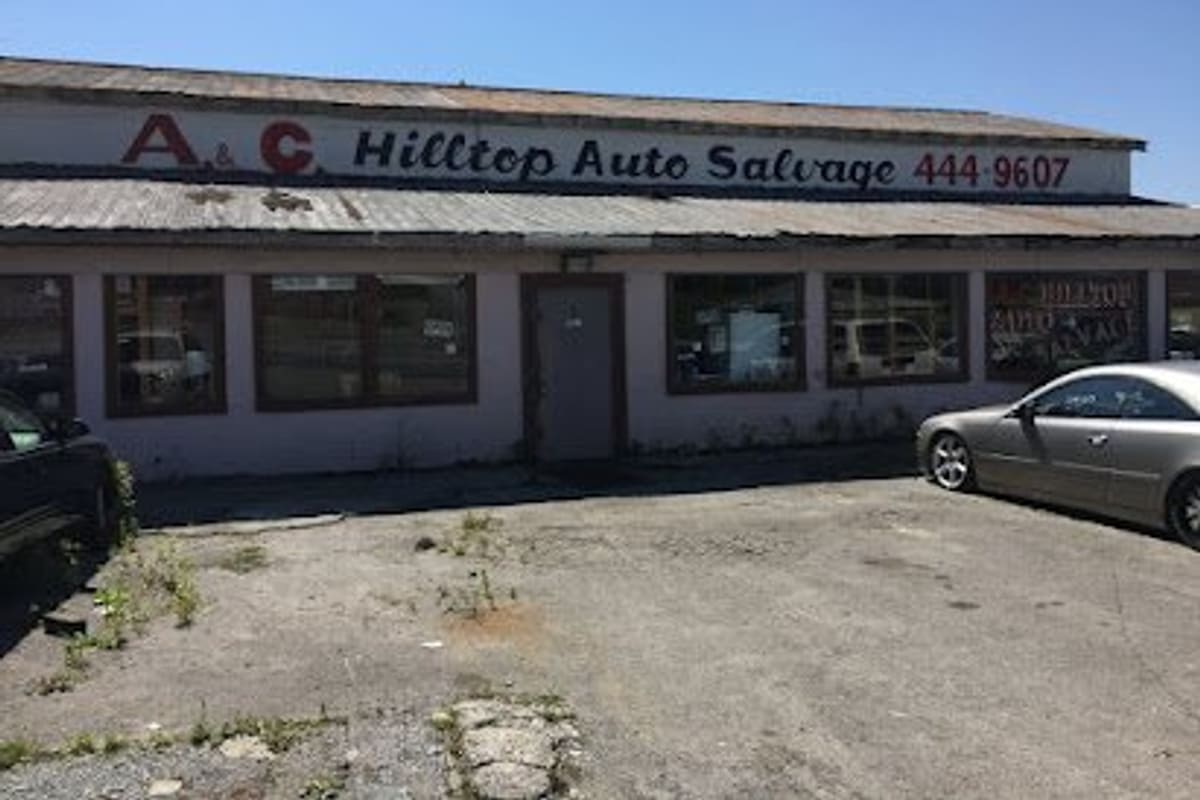 A. C. Hilltop Auto Salvage: Single-story salvage shop building with a painted sign above the storefront and a paved lot with parked cars in front