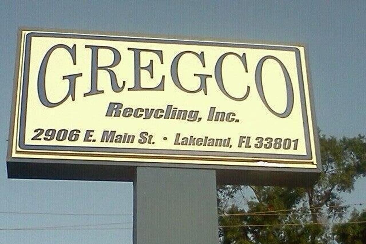 Gregco Recycling: Tall roadside pole sign with business name and street address in Lakeland, Florida, against a blue sky and trees
