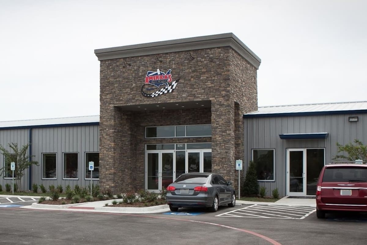 Americas Auto Auction: Gray metal building with a tall stone entrance tower, a logo above the glass doors and cars parked out front