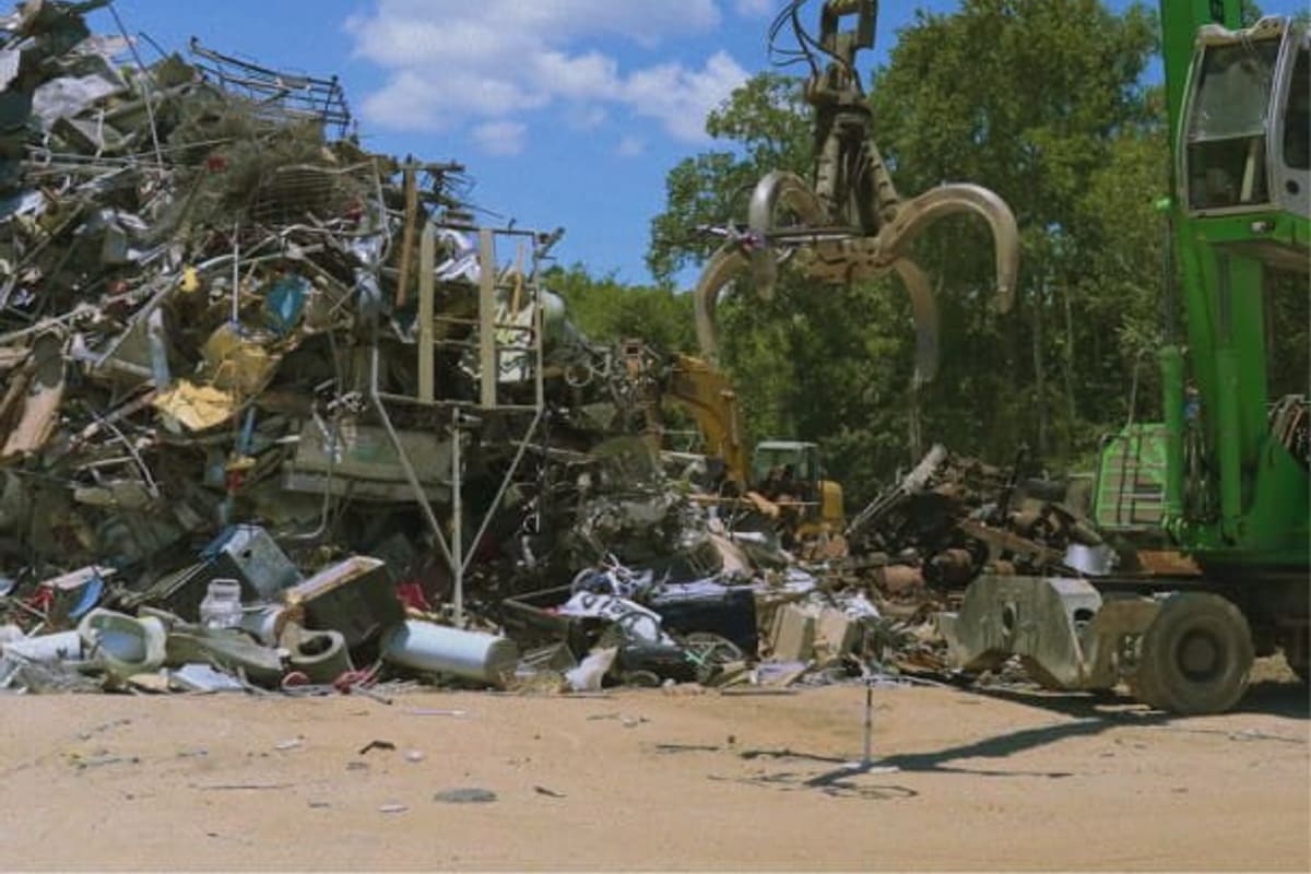 Iron Ranch Recycling: Green material handler with grapple claw beside a large pile of scrap metal at a recycling yard