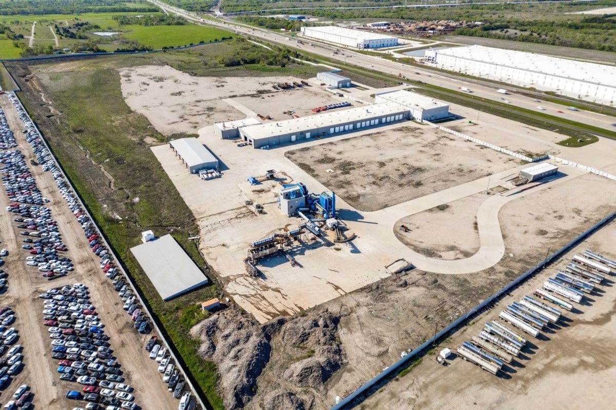 Usar: Aerial view of a large salvage lot with rows of parked cars, industrial buildings and equipment beside a highway