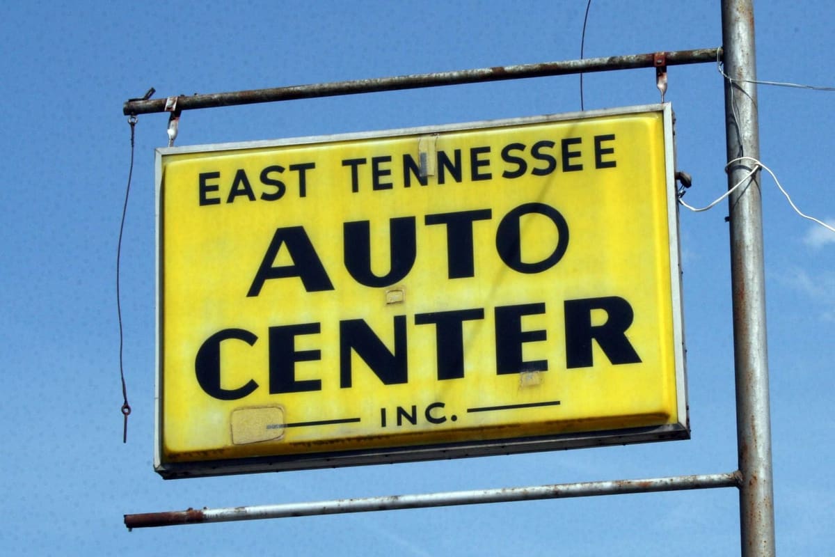 East Tenn. Auto Center: Yellow hanging road sign reading East Tennessee Auto Center Inc. on a rusty pole against a blue sky