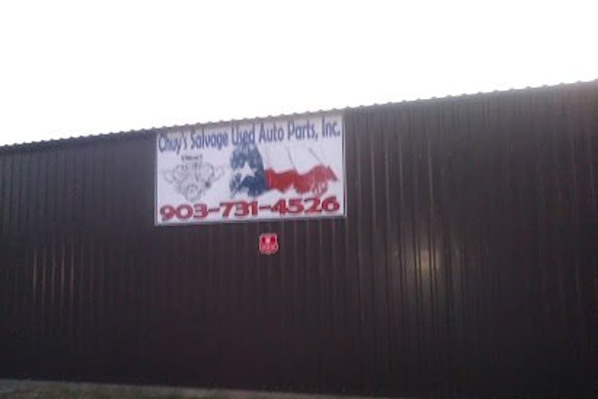 Chuy's Salvage Used Auto Parts: Banner sign with Texas flag and phone number mounted on a dark corrugated metal building