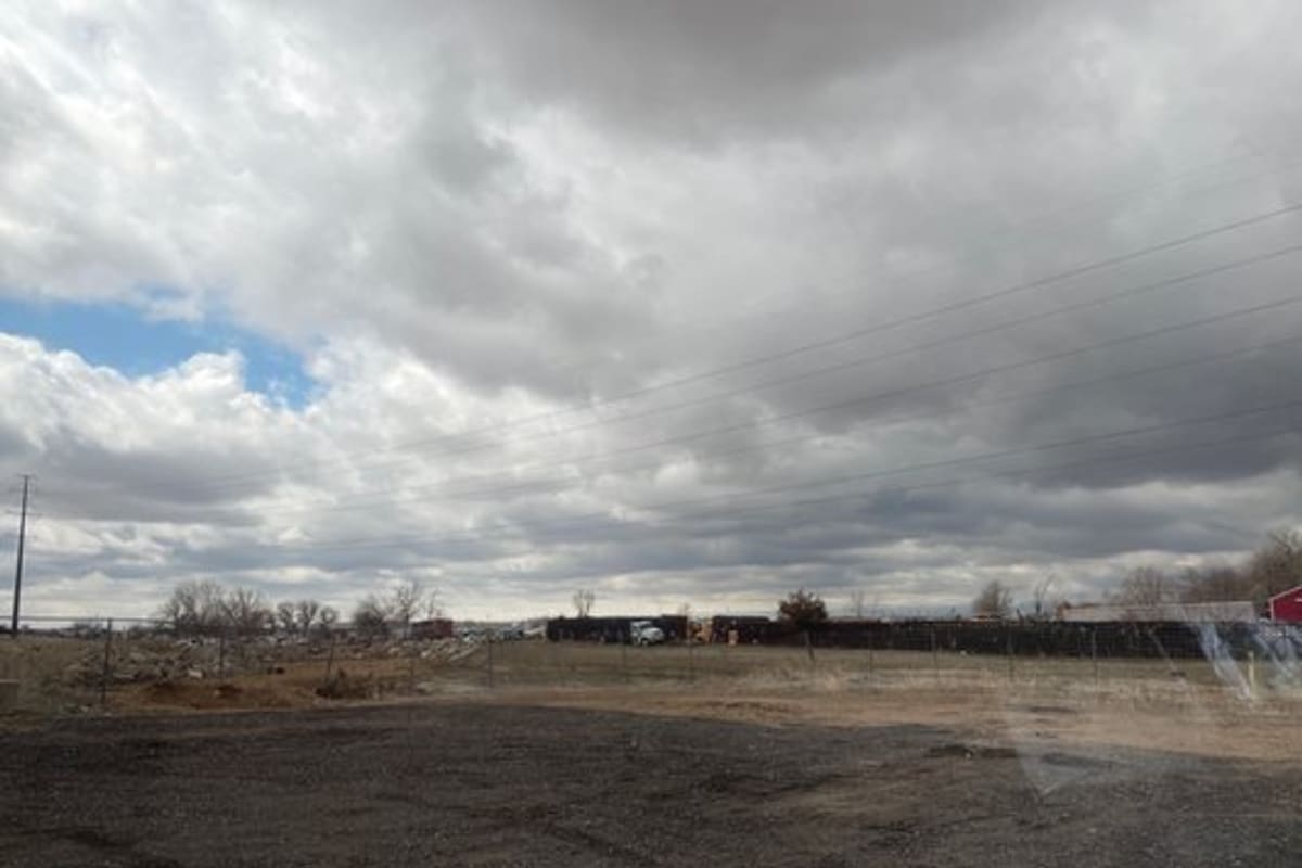 Erie Auto Salvage: Gravel lot with fenced yard and vehicles in the distance under a cloudy sky
