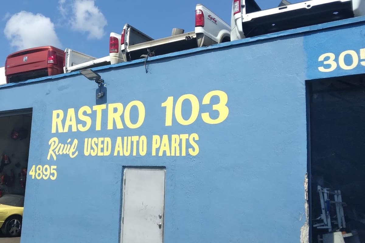 103 Used Auto Parts: Blue used auto parts building with painted yellow lettering, a street sign, and truck beds stacked on the roof