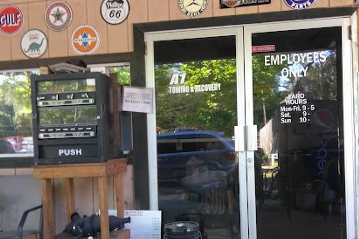 McKee Wrecker & Salvage: Glass double doors of a salvage office entrance with vintage signs above and a vending machine on a wooden stand