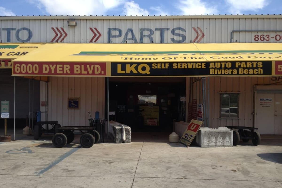 LKQ Pick Your Part: Yellow awning over the open entrance of a self-service auto parts yard, with wheeled carts and concrete blocks out front