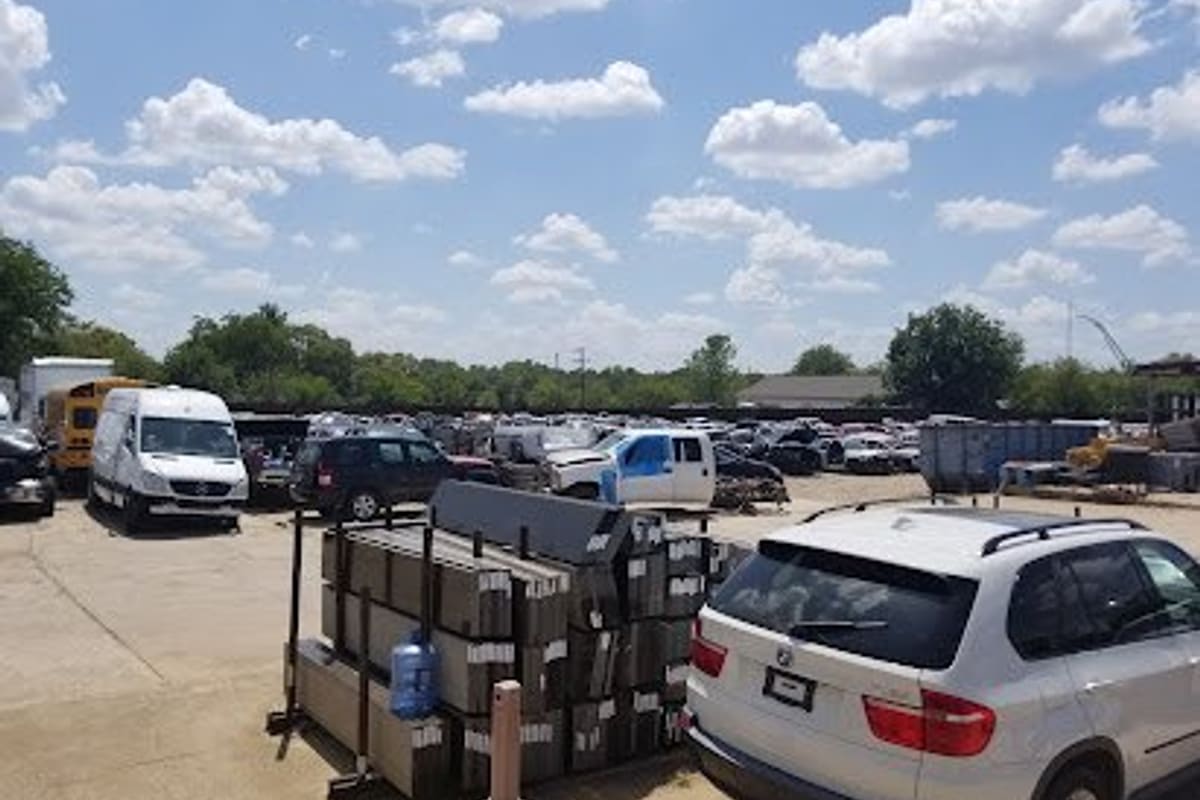 Action Auto Recycling: Wide daytime view of a salvage yard lot with many vehicles, a white SUV, and stacked parts under a partly cloudy sky