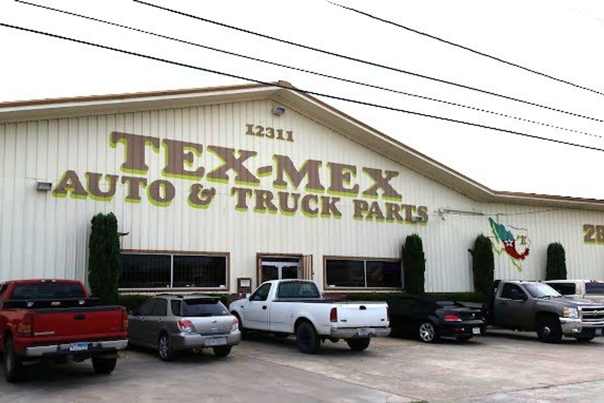 Tex Mex Used Auto Parts Trucks: Large cream metal building with a painted Tex-Mex Auto & Truck Parts sign and pickup trucks parked in front