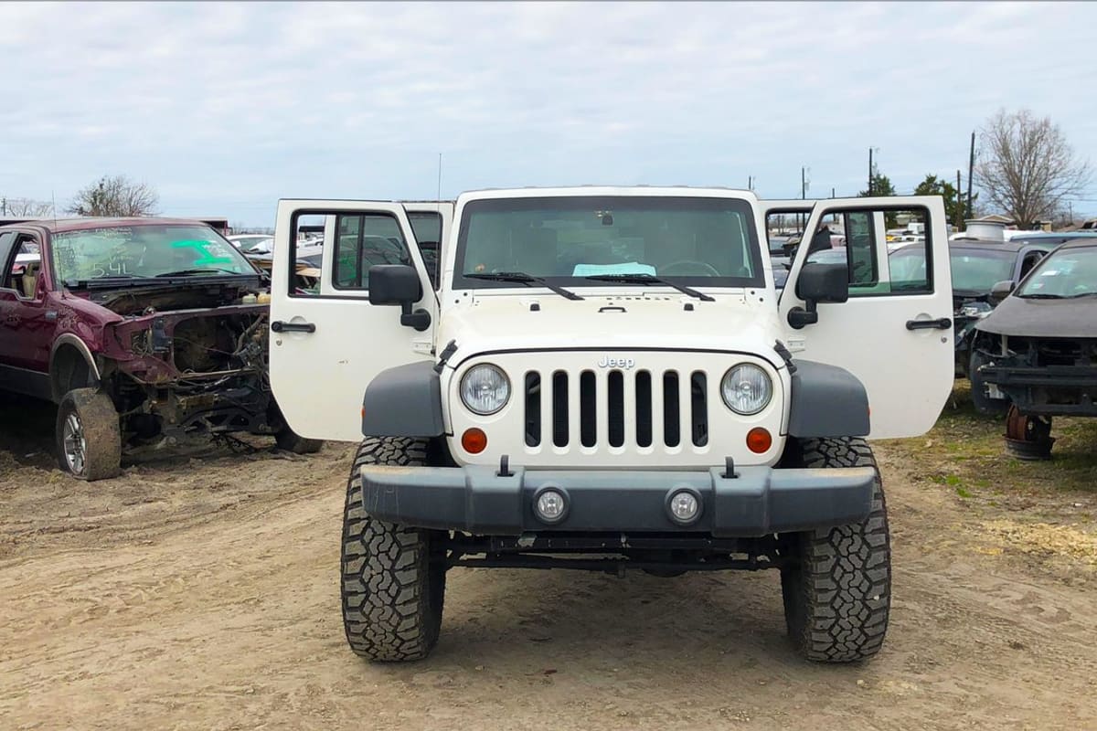 Special Truck and Auto Salvage: Salvage yard with a white Jeep, doors open, parked among rows of wrecked vehicles on a dirt lot