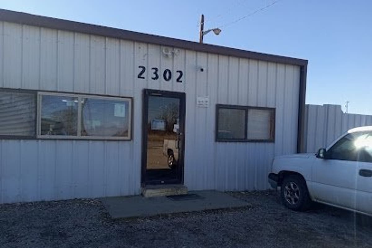 Highway 77 Auto Salvage: Metal office building with house number 2302 above a glass door and a white pickup parked on gravel out front