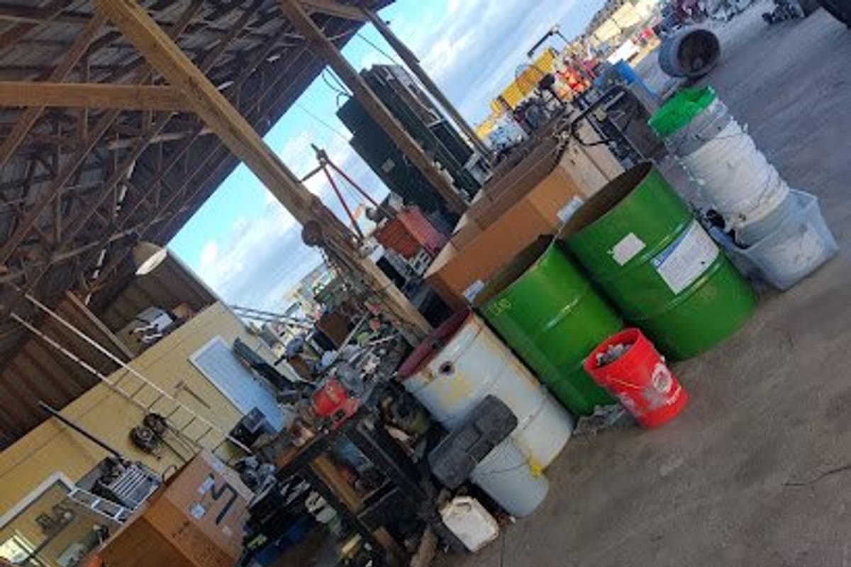 Jim's Auto Salvage: Covered work area at a salvage yard with barrels, buckets, scrap and equipment under a wooden roof frame