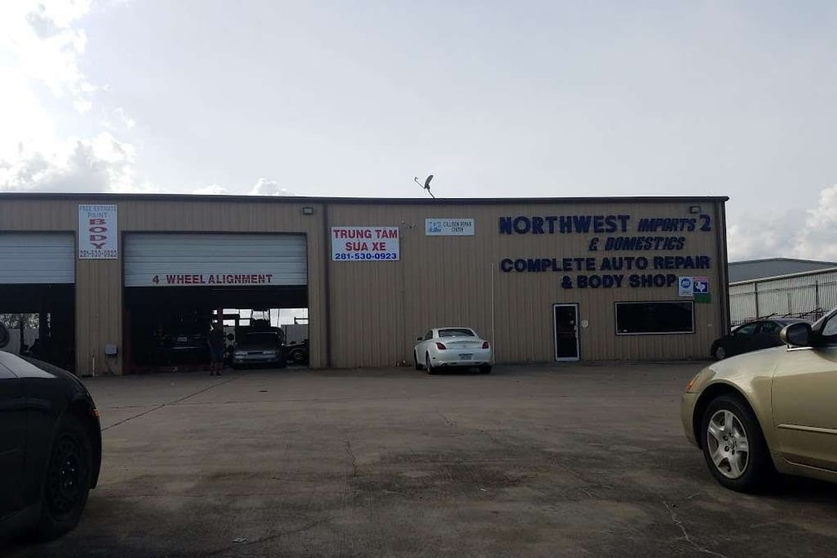 Northwest Imports 2: Tan metal auto repair shop building with bay doors, blue signage and a paved parking lot in front