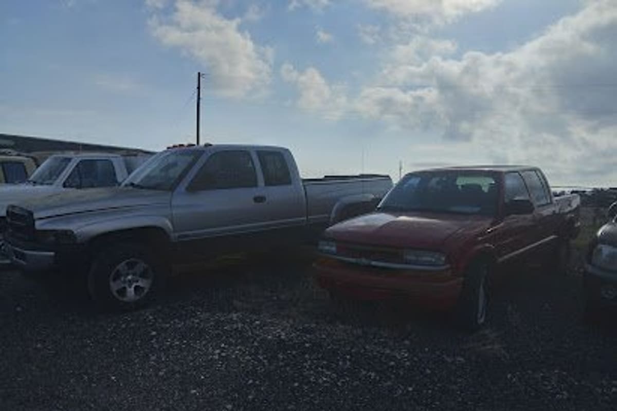 Anderson Auto Salvage: Pickup trucks parked on a gravel lot under a partly cloudy sky