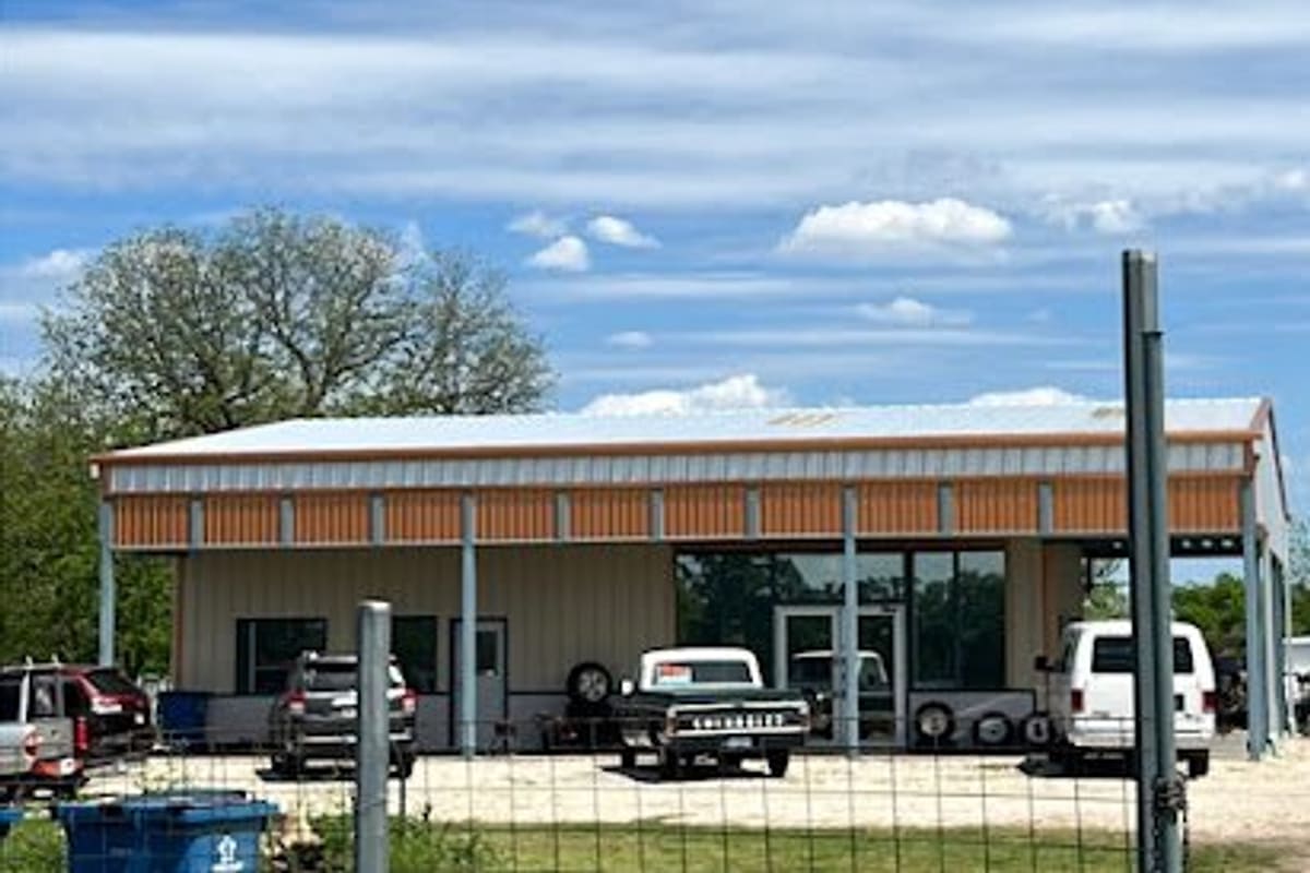 Quality 5 Auto Recyclers: Metal shop building with orange and tan siding, vehicles and spare tires parked out front behind a wire fence