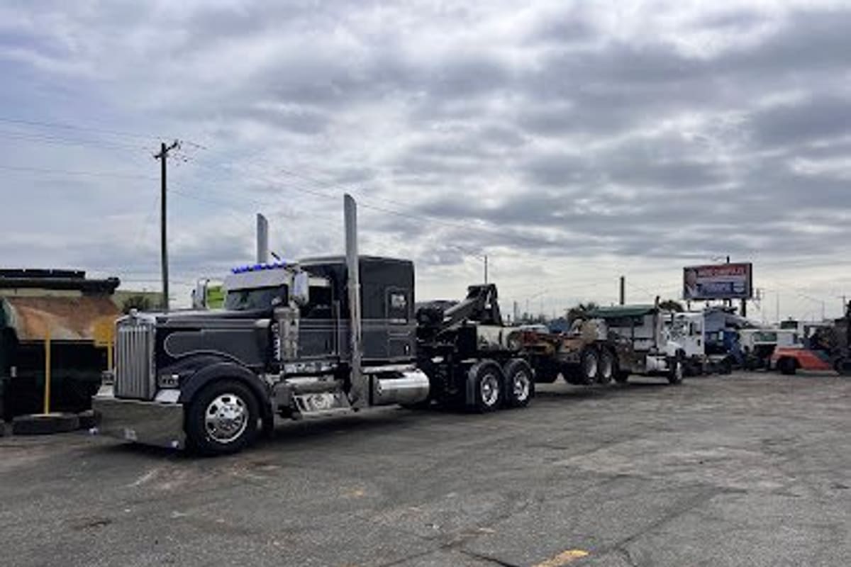 Go Trucks & Parts: Black semi tow truck parked on a paved lot with other heavy trucks and a billboard in the background