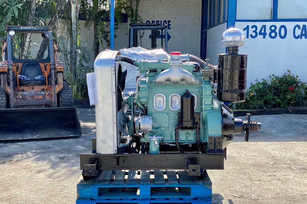C.a. Truck Parts: Engine on a blue pallet in front of a building with an office sign and street number, with a skid steer to the left