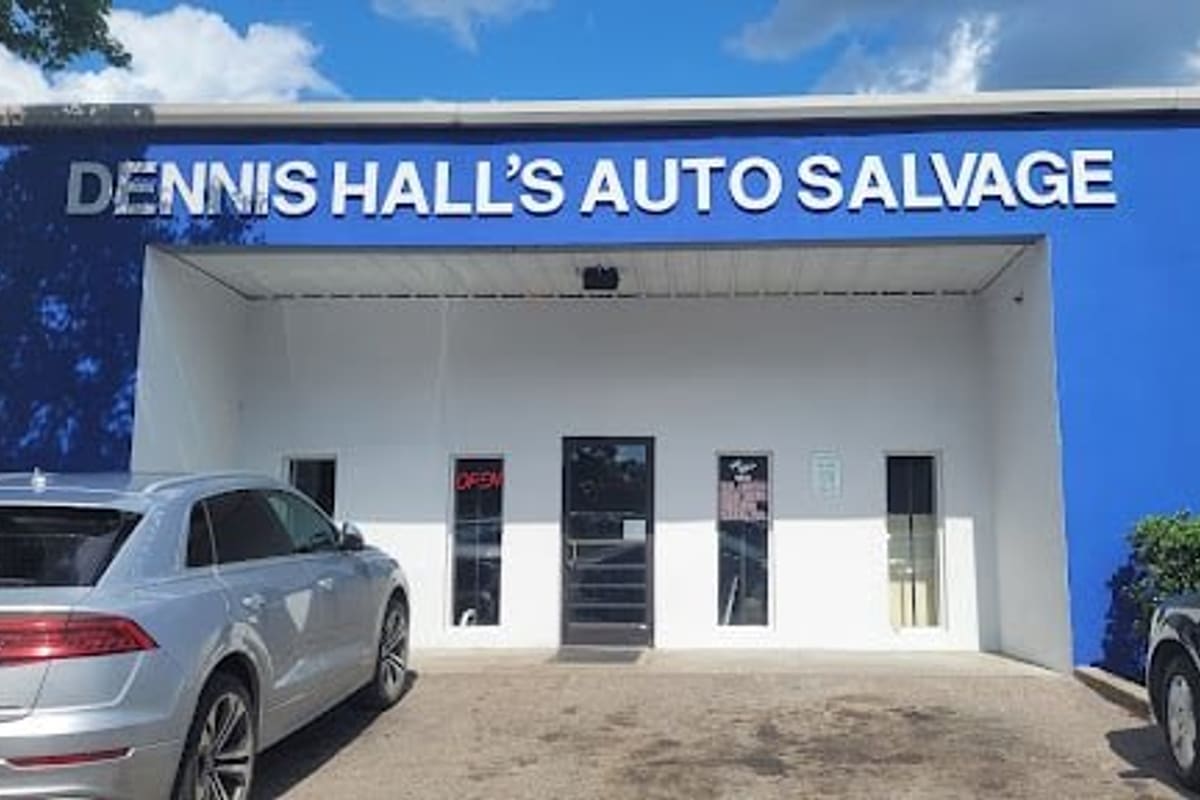 Dennis Hall's Auto Salvage: Blue and white building with a covered entrance, glass door and open sign, with cars parked in front