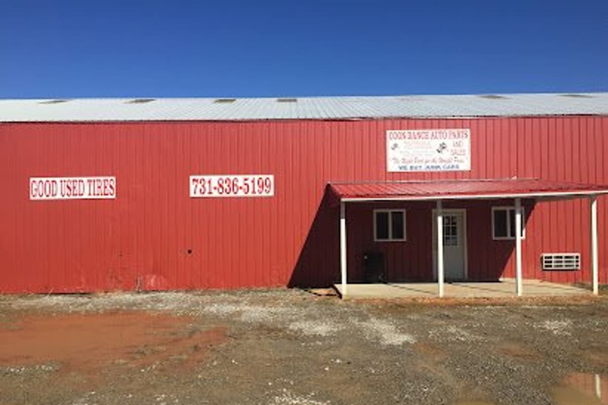 Coon Dance Auto Parts: Large red metal building with a covered entrance porch, painted signs for good used tires and a phone number, and a gravel lot in front
