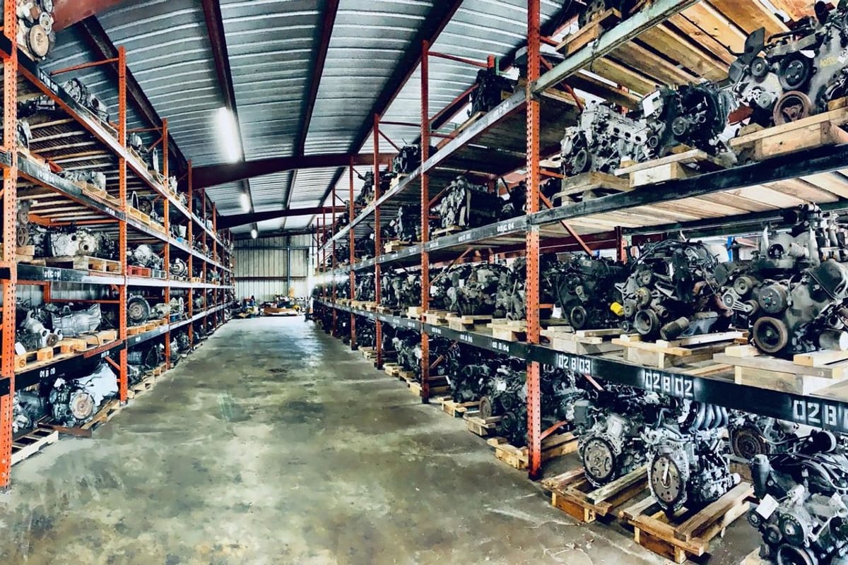 Action Auto Recycling: Warehouse aisle with tall orange racks holding rows of used engines and transmissions on wooden pallets