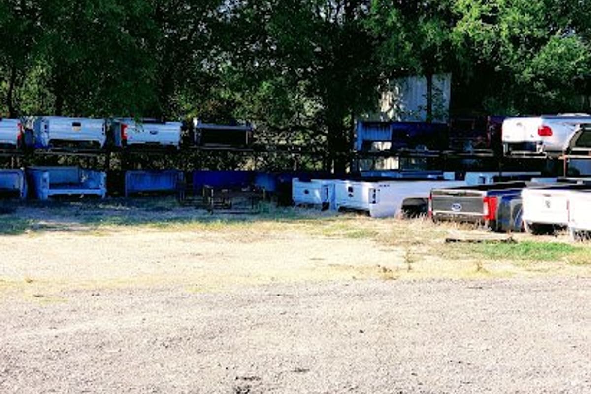Quinton & Sons Auto Parts and Auto Glass: Gravel lot with rows of pickup truck beds stacked on racks in front of trees on a sunny day