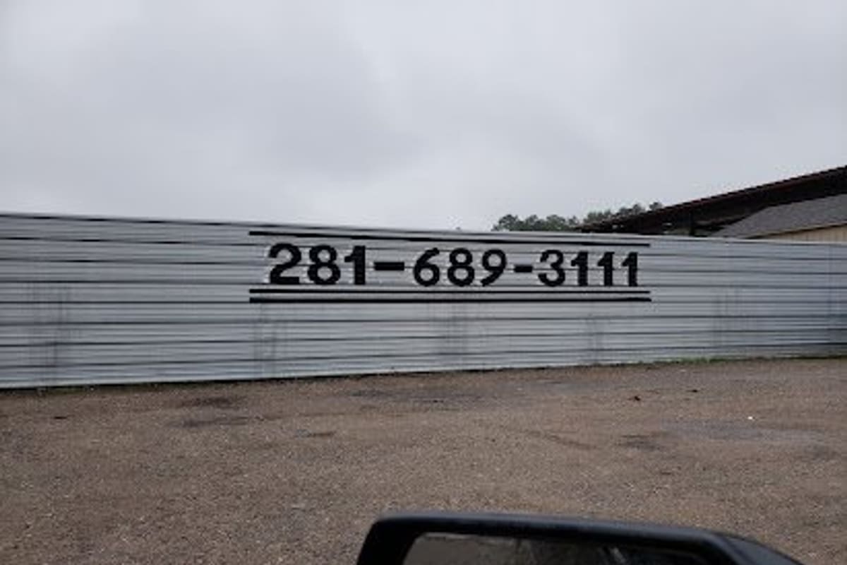 Dixie Used Auto Parts: Long corrugated metal fence painted with a large phone number, beside a gravel lot under an overcast sky
