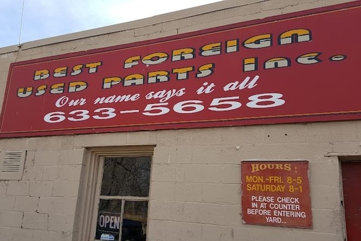 Best Foreign Used Parts: Red storefront sign with phone number above a cinder block wall, an open door and a posted hours notice