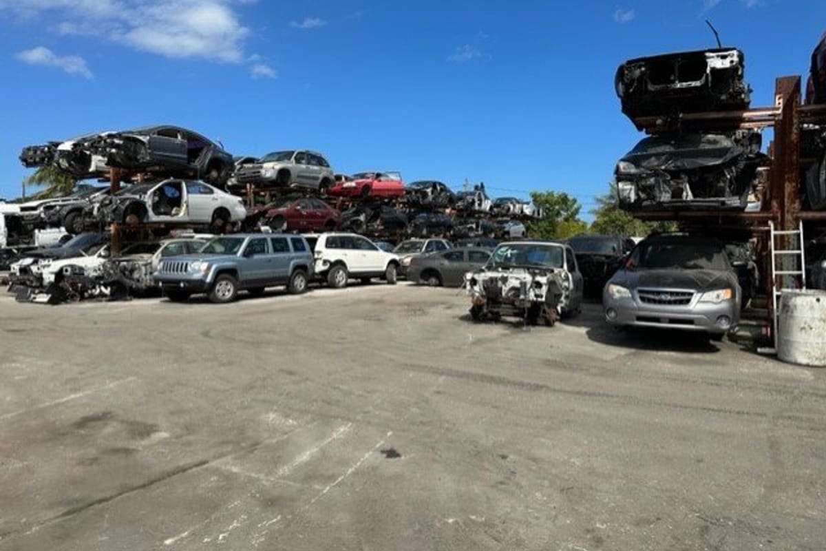 Affordable Foreign & Truck Salvage: Wide view of a salvage yard with stacked wrecked cars and rows of vehicles on a paved lot under a blue sky
