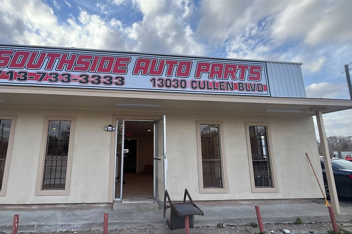 Southside Auto Parts: Single-story stucco storefront with a large red and white sign above an open glass door and barred windows under a cloudy sky