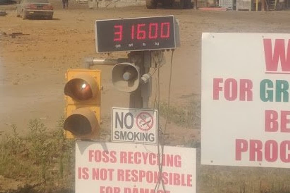 Foss Recycling: Dusty recycling yard with conveyor and processing equipment behind a scale readout, traffic light and warning signs