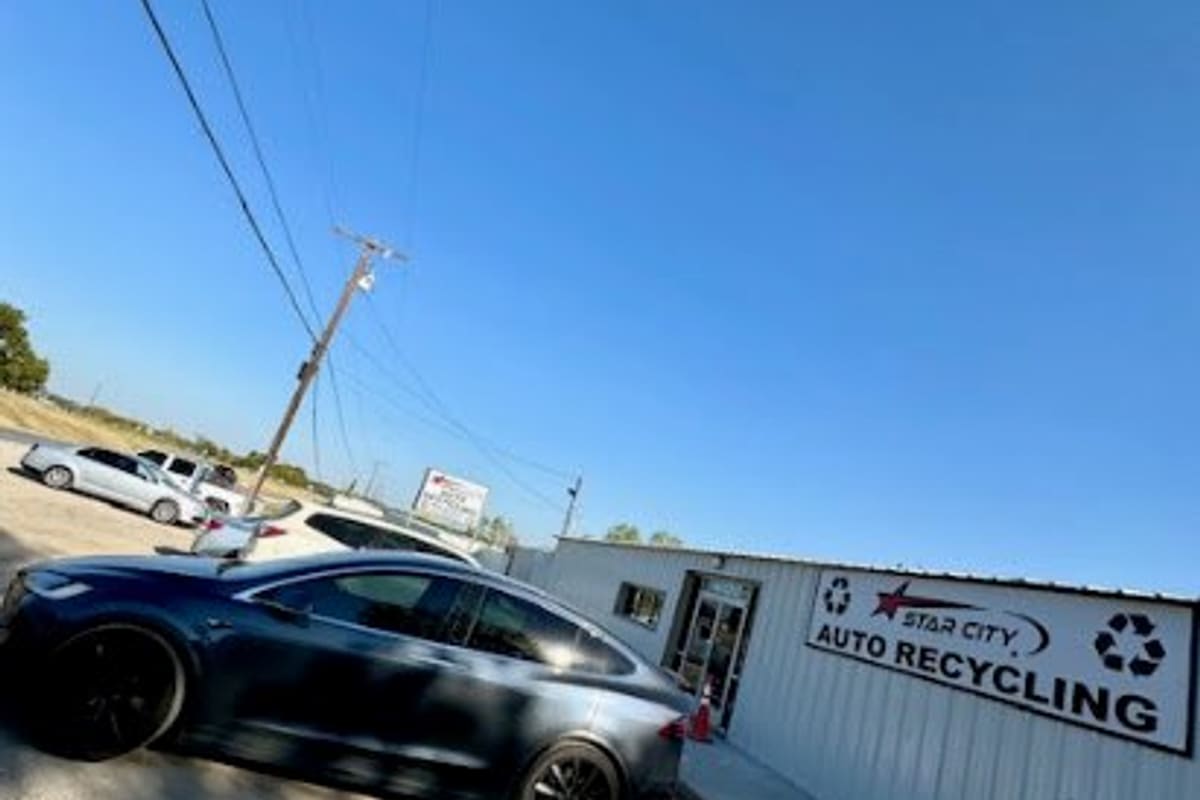 Star City Auto Recyclers: Metal office building with a large auto recycling sign beside a gravel lot with cars parked under a clear blue sky