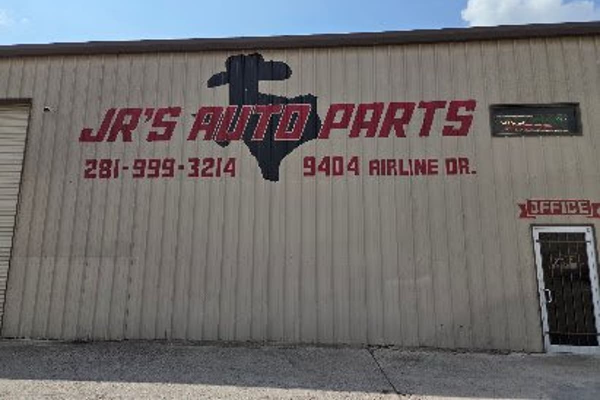 Jr's Auto Parts: Tan metal warehouse wall painted with red lettering, a Texas silhouette, phone number, street address and an office door