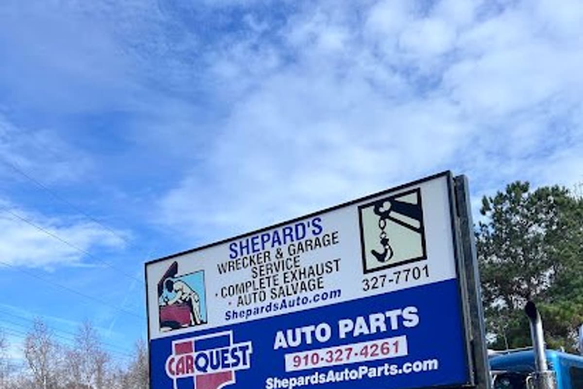 Shepard's Wrecker & Garage Services: Large roadside sign for wrecker service, auto parts and salvage beside a blue tow truck on a grassy lot