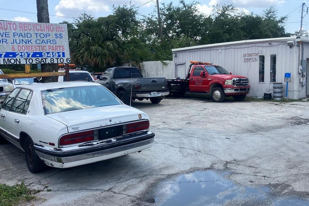 Papi's Recycling: Gravel lot with parked cars, a red tow truck and a small white shop building with tires stacked by the door