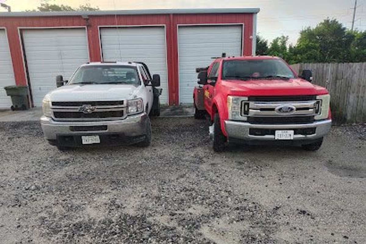Johnny's Towing & Recovery: Two flatbed tow trucks parked on a gravel lot in front of a red metal building with white garage doors