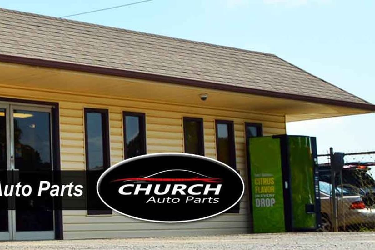 Church Auto Parts: Single-story yellow office building with a covered entrance, glass double doors, and chain-link fence beside a salvage yard