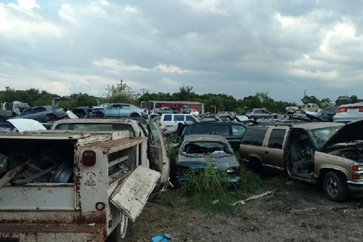 Austin Express Auto Parts: Wide view of a salvage yard with rows of old cars and trucks on dirt ground under a cloudy sky