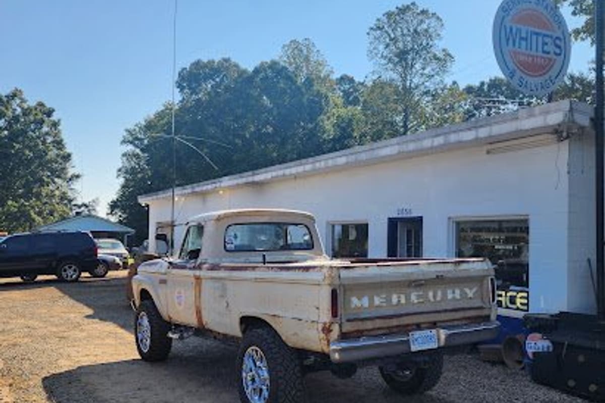 White's Service Station & Garage: White building with a round service station and salvage sign, an old pickup truck parked on the gravel lot in front