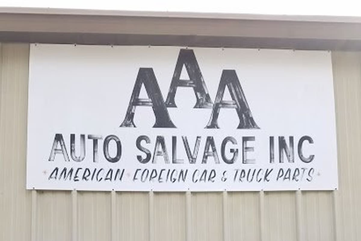 AAA Auto Salvage: Large white sign reading AAA Auto Salvage Inc, American and foreign car and truck parts, on a metal building above shrubs