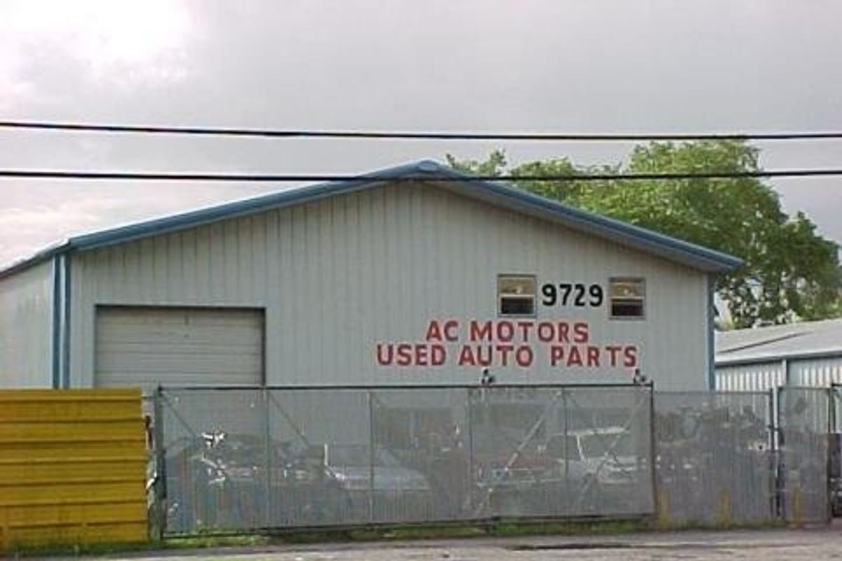 Comanche Auto Parts: Gray metal warehouse building with a roll-up door, address 9729 and a chain-link fence with vehicles behind it