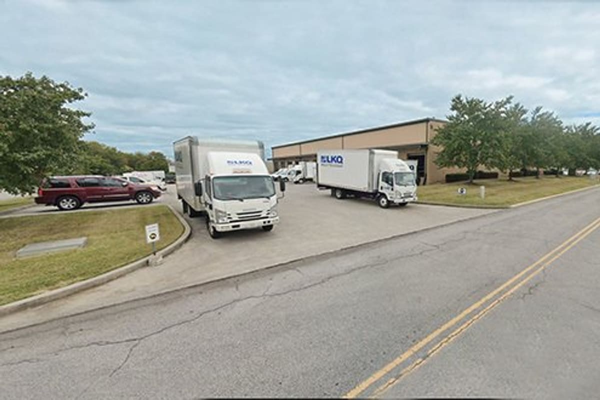 LKQ Knoxville TN: Tan warehouse building with box trucks parked in the driveway beside a street